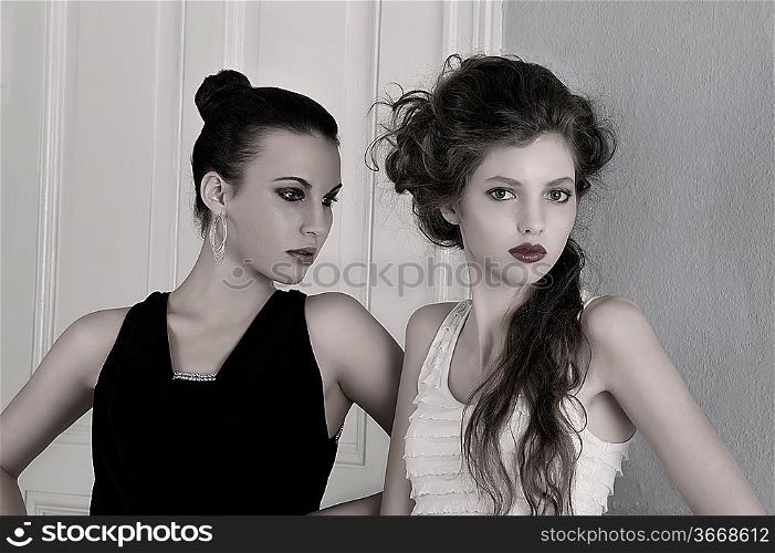 two beautiful girls with amazing styles and elegant dresses posing indoor near an old fashion door posing with attractive poses and attitude towards the camera