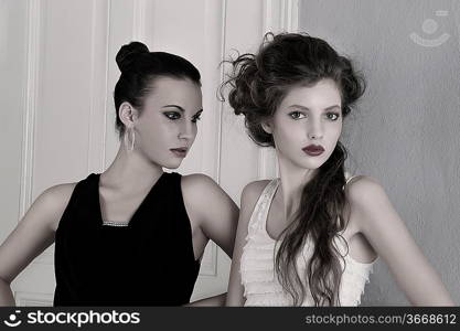 two beautiful girls with amazing styles and elegant dresses posing indoor near an old fashion door posing with attractive poses and attitude towards the camera