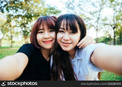 Two beautiful happy young asian women friends having fun together at park and taking a selfie. Happy hipster young asian girls smiling and looking at camera. Lifestyle and friendship concepts.