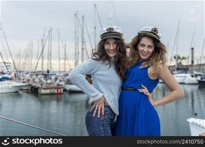 Two beautiful model women standing and posing on a sailboat while looking at camera smiling