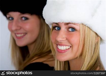 Two beautiful Russian women wearing fur hats, shot in three quarter profile, one in focus one out but both smiling for the camera