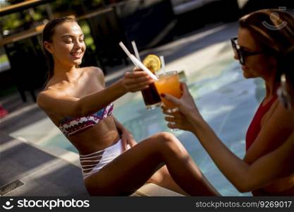 Two beautiful slim young women in bikini relaxing and drink cocktails on poolside of a swimming pool