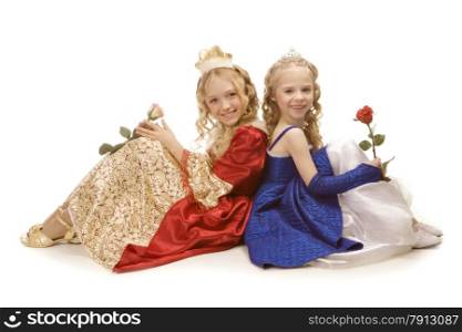 Two beautiful smiling little girls with long blonde hair in the princess costumes sitting on the floor with two roses. Red and blue empire dresses