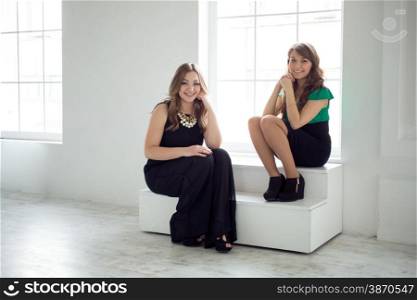 Two beautiful stylish girls sitting on windowsill
