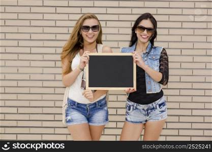 Two beautiful teenage friends having fun and holdign a chalkboard