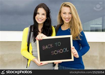 Two beautiful teenage students holding a chalkboard with the slogan Back to School