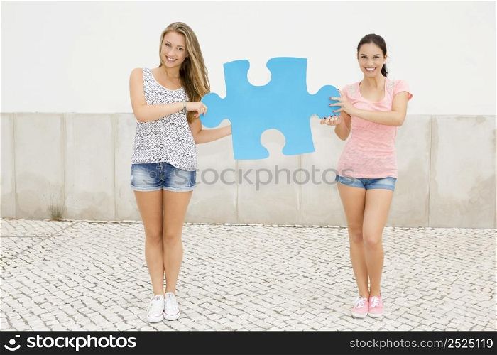 Two beautiful teenage students holding a giant puzzle piece