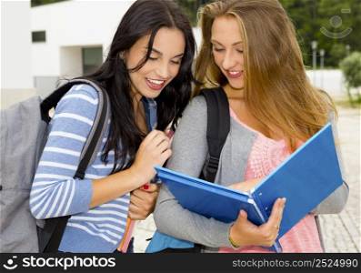 Two beautiful teenage students studying and showing something in the books