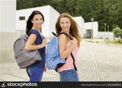 Two beautiful teenage students walking while looking back and smiling