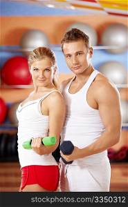 Two beautiful trainers with dumbbells in hands in sports club