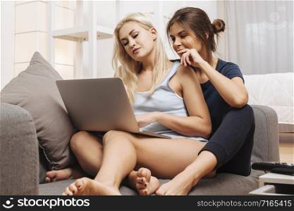 Two beautiful women in a relationship sitting on a sofa using a laptop together.