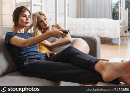 Two beautiful women in a relationship sitting on a sofa watching television.