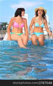 two beautiful women sitting on ledge pool open-air