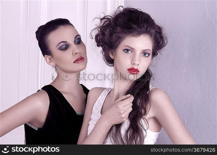 two beautiful women with hair style and elegant dress posing indoor near an old fashion door posing with attitude