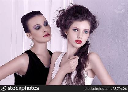 two beautiful women with hair style and elegant dress posing indoor near an old fashion door posing with attitude