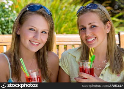 Two beautiful young blond women drinking cocktails outside during a warm summer day
