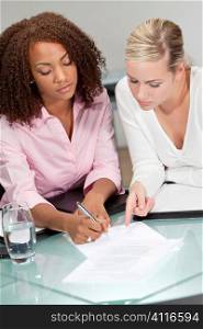 Two beautiful young businesswomen or lawyers, one African American one caucasian, discussing and signing a contract or legal document