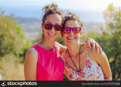 Two beautiful young woman female girl friends or sisters having fun in nature outdoors hugging embracing each other smiling wearing summer dress sunglasses in the autumn travel