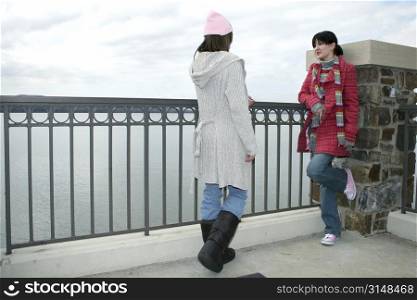 Two beautiful young woman in winter clothes outside at the lake talking on a cold hazy day.