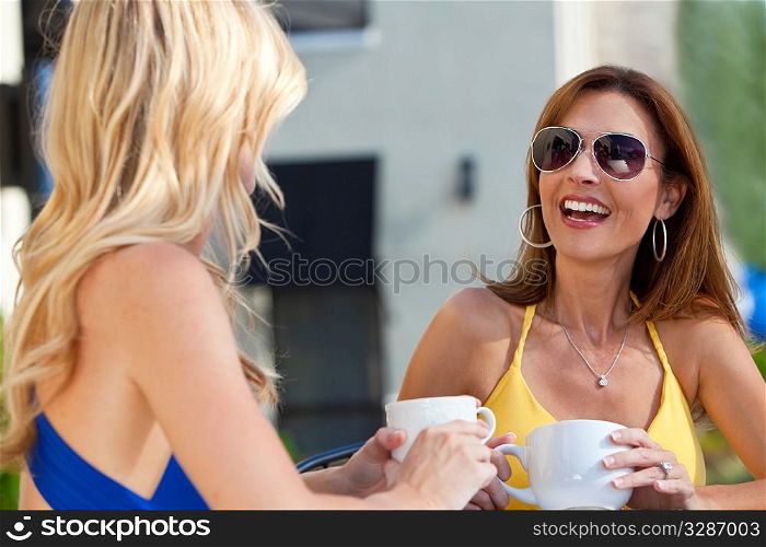 Two beautiful young woman outside at a city cafe laughing and drinking coffee