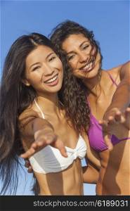 Two beautiful young women in bikinis having fun laughing and dancing partying together on a sunny beach with blue sky