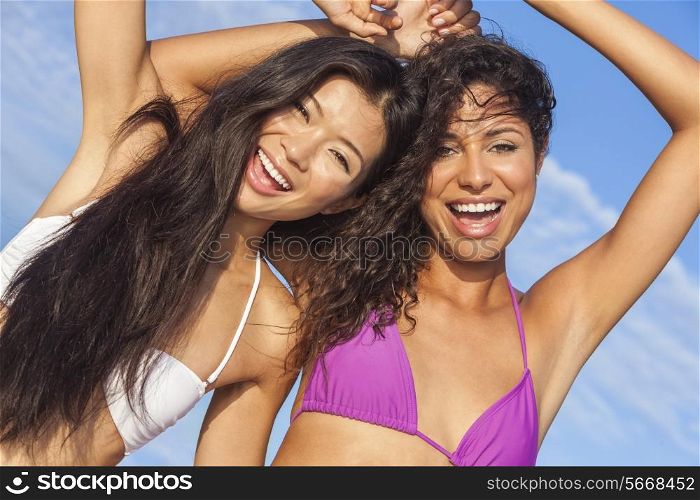Two beautiful young women or girls, Asian and Latina Hispanic, in bikinis dancing on vacation on a hot sunny beach