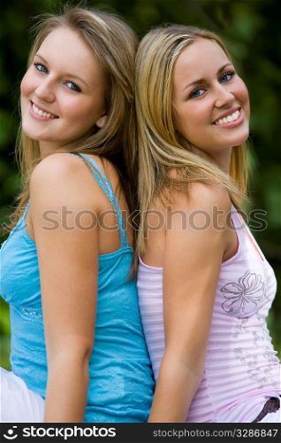 Two beautiful young women sitting back to back in the summer sunshine