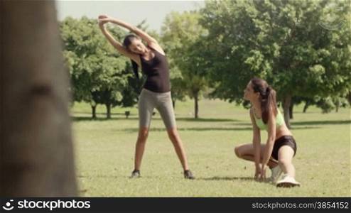Two beautiful young women stretching muscles in city park after running and doing sport activity. Dolly shot