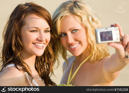 Two beautiful young women taking pictures of themselves at the beach