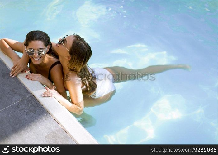 Two beautiful young Women with sunglasses relaxing together by poolside of outdoor swimming pool and smiling