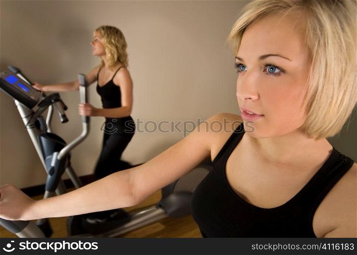 Two beautiful young women working ot on cross training machines at the gym