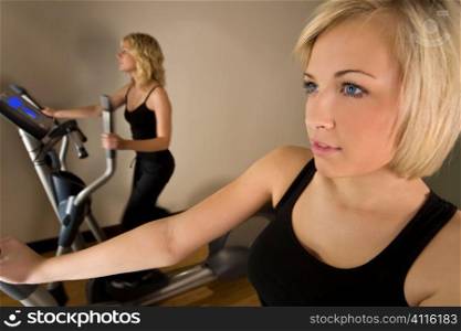 Two beautiful young women working ot on cross training machines at the gym