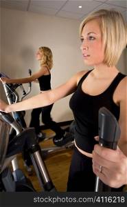 two beautiful young women working ot on cross training machines at the gym