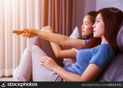 two best friends watching tv with remote on sofa in living room at home