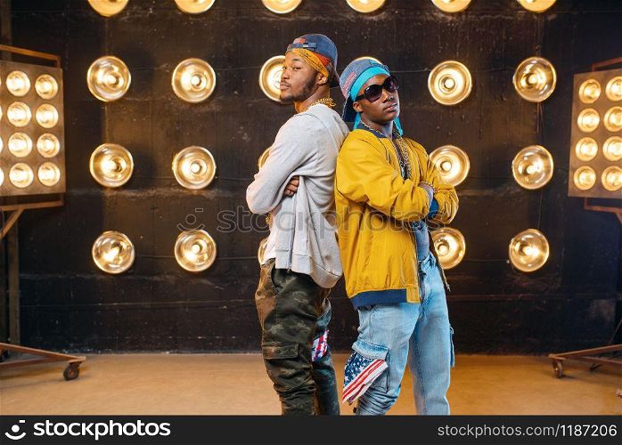 Two black rappers, dance perfomance on stage with spotlights on background. Rap singers on scene with lights, underground music concert, urban style. Two black rappers, dance perfomance on scene