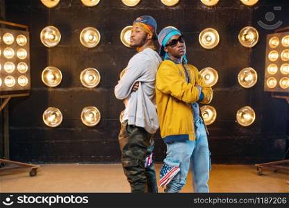 Two black rappers, dance perfomance on stage with spotlights on background. Rap singers on scene with lights, underground music concert, urban style. Two black rappers, dance perfomance on scene