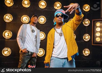 Two black rappers in caps on stage with spotlights on background. Rap performers on scene with lights, underground music, urban style