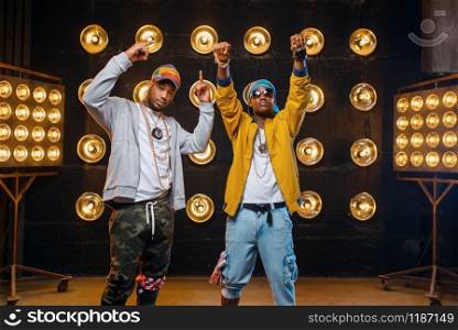 Two black rappers in caps, perfomance on stage with spotlights on background. Rap performers on scene with lights, underground music concert, urban style. Two black rappers in caps, perfomance on stage