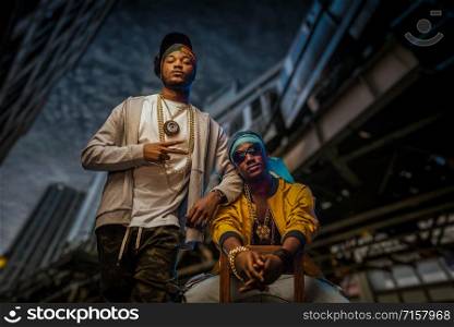 Two black rappers poses on night city street, skyscrapers on background. Rap performers against cityscape, underground music concert, urban style