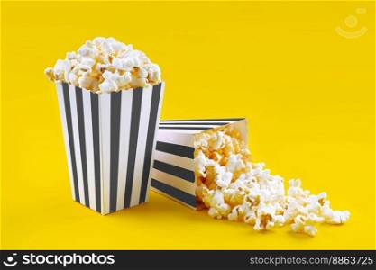 Two black white striped carton buckets with tasty cheese popcorn, isolated on yellow background. Box with scattering of popcorn grains. Movies, cinema and entertainment concept.