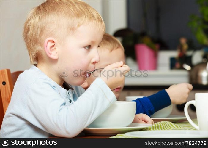 Two blond brothers boys kids children eating corn flakes breakfast morning meal at the table. Home.