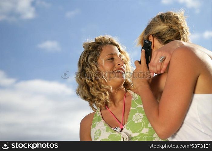 Two blond friends making a call whilst at the beach