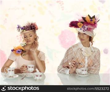 two blonde girl with floral decoration and classical tea set on the table, they have old style fashion hat