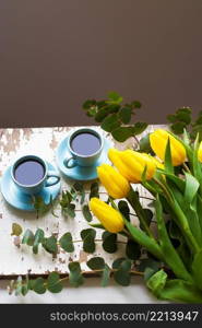 two blue cup of coffee with yellow tulips on an old table. freshly brewed coffee