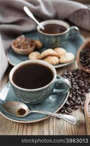 Two blue cups of black coffee, cookies and sugar pieces surrounded by linen cloth on old wooden table