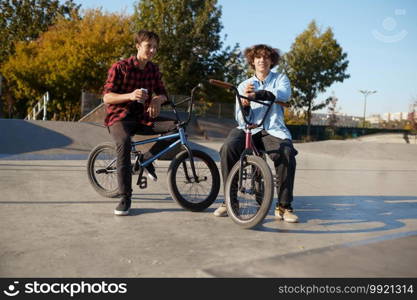 Two bmx bikers poses on r&in skatepark. Extreme bicycle sport, dangerous cycle exercise, street riding, biking in summer park. Two bmx bikers poses on r&in skatepark