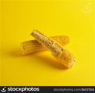 two boiled corncob lies on a yellow background, one is bitten