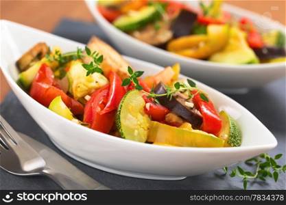 Two bowls of fresh homemade Ratatouille made of eggplant, zucchini, bell pepper and tomato and seasoned with herbs (garlic, thyme, oregano) (Selective Focus, Focus on the front leaves of the thyme sprig on the meal). Ratatouille