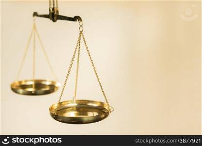 Two bowls of scales made of golden metal suspended on chains on a beige background