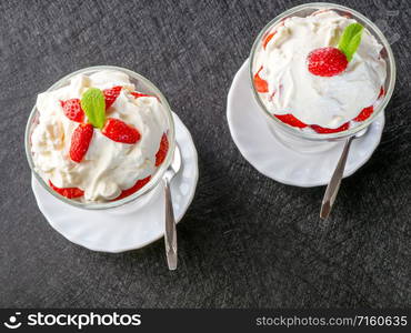 Two bowls with strawberries and whipped cream/ Top view. Two bowls with strawberries and whipped cream on a dark background